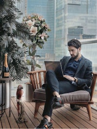a man sitting on a chair with a laptop and a bottle of wine